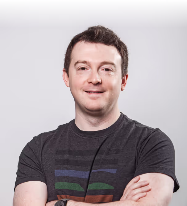 Michael Balyasny smiling with arms crossed in a dark t-shirt against a grey studio wall